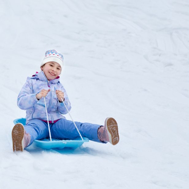 Concept of childhood, sledding in winter. Happy little girl is rolling down the hill on a sled. Happy holidays.